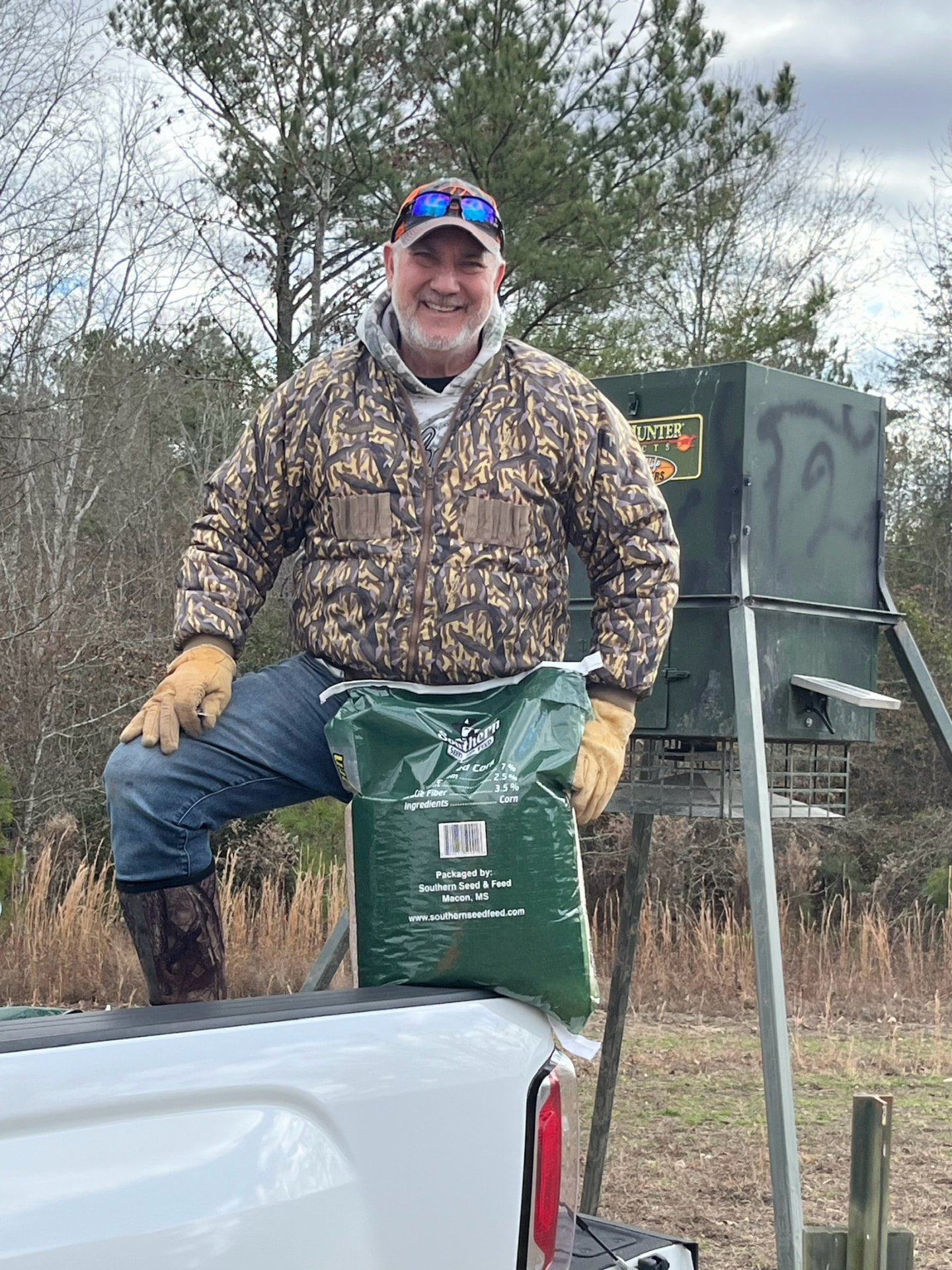 JB Barber with a bag of Southern Seed & Feed corn by a tripod feeder at the ranch